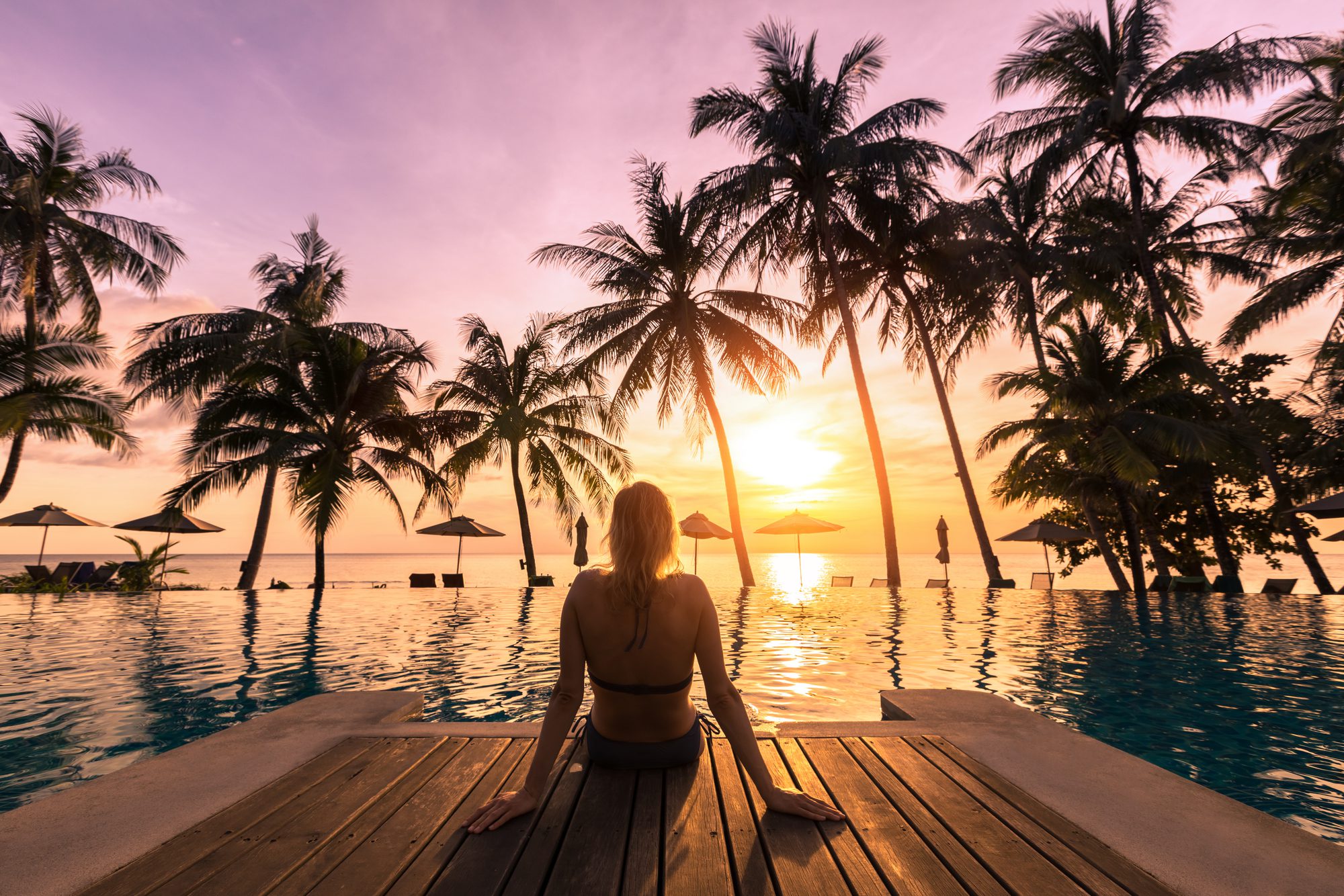Woman relaxing by the pool in a luxurious beachfront hotel resort at sunset
