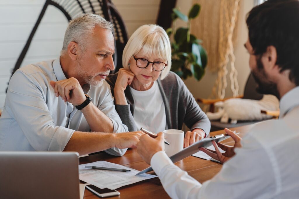 Older clients consulting agent, broker about house selling, medical insurance terms, trust fund investment, meeting at laptop in office. Senior couple discussing wills with lawyer, solicitor, notary